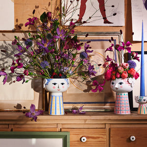 To Bjørn Wiinblad Eva vaser fylt med blomster, står på en hylle blant kunstverk, som ønsker en kreativ atmosfære.