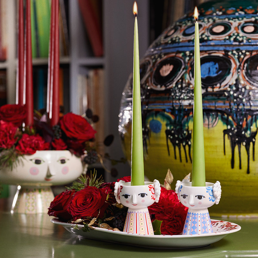 To Bjørn Winblad Eva lysestaker dekorert med grønne lys, plassert på et dekorativt fat med røde roser.