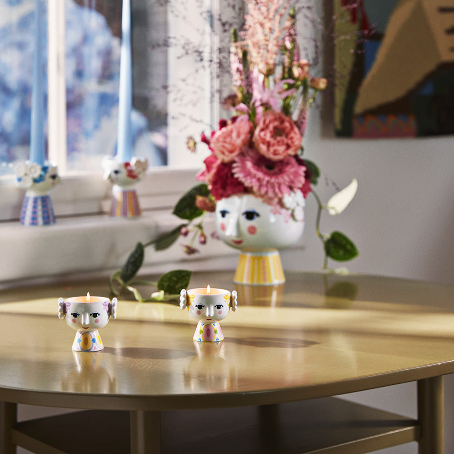 Bjørn Wiinblad telysholdere plassert på et bord med blomster, viser den kreative og fargerike stilen som beriker hjemmet.