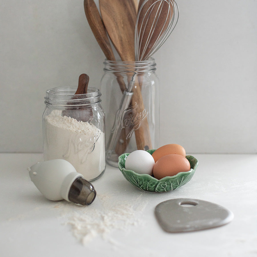Grå deigskrape på kjøkkenbenk med mel, egg og bakeutstyr