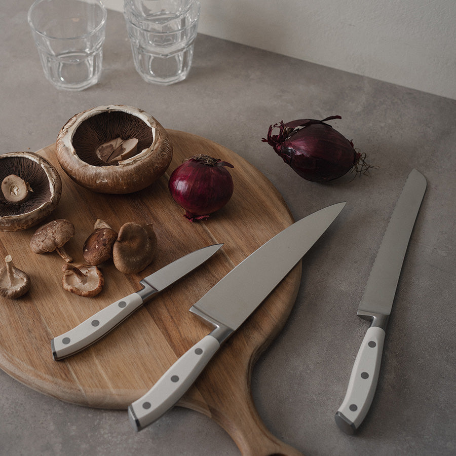 Christiania 1739 Culinary Knivsett 3 Deler Hvit på en skjærebrett med grønnsaker, og viser det elegante designet og funksjonaliteten til knivsettet.