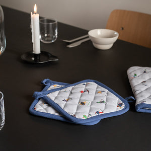 Christiania Glasmagasin gryteklut med lekent skiprint, 20x20 cm, perfekt til kjøkkenet, viser både grytekluter på et mørkt bord med lys og serveringsutstyr.