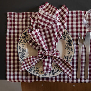 Borddekkning med burgunder rutet tøyserviett, elegant brettet rundt en tallerken med blomsterdekor. Perfekt for en stilig middag.