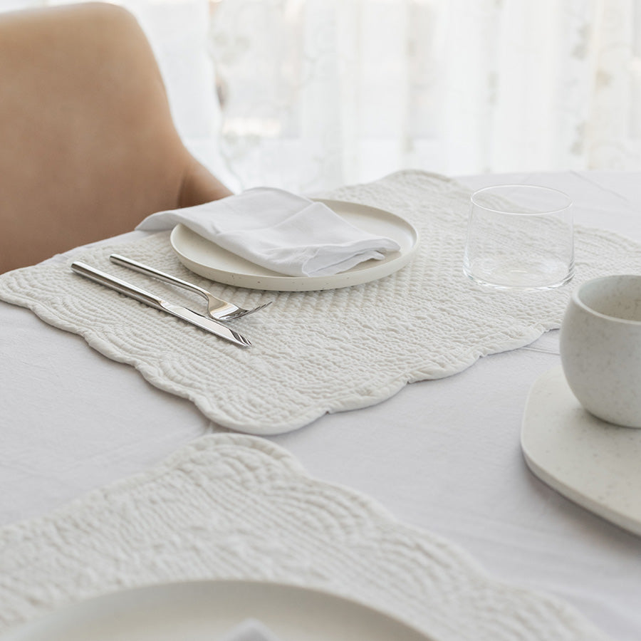 Nærbilde av hvit dekkebrikke i quiltet bomull, med en tallerken og bestikk. Ideell for en minimalistisk og elegant bordoppsett.