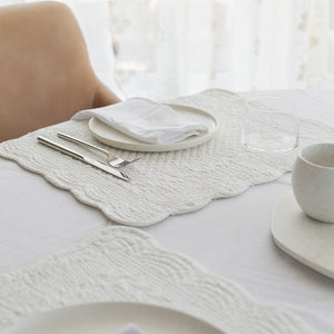 Nærbilde av hvit dekkebrikke i quiltet bomull, med en tallerken og bestikk. Ideell for en minimalistisk og elegant bordoppsett.