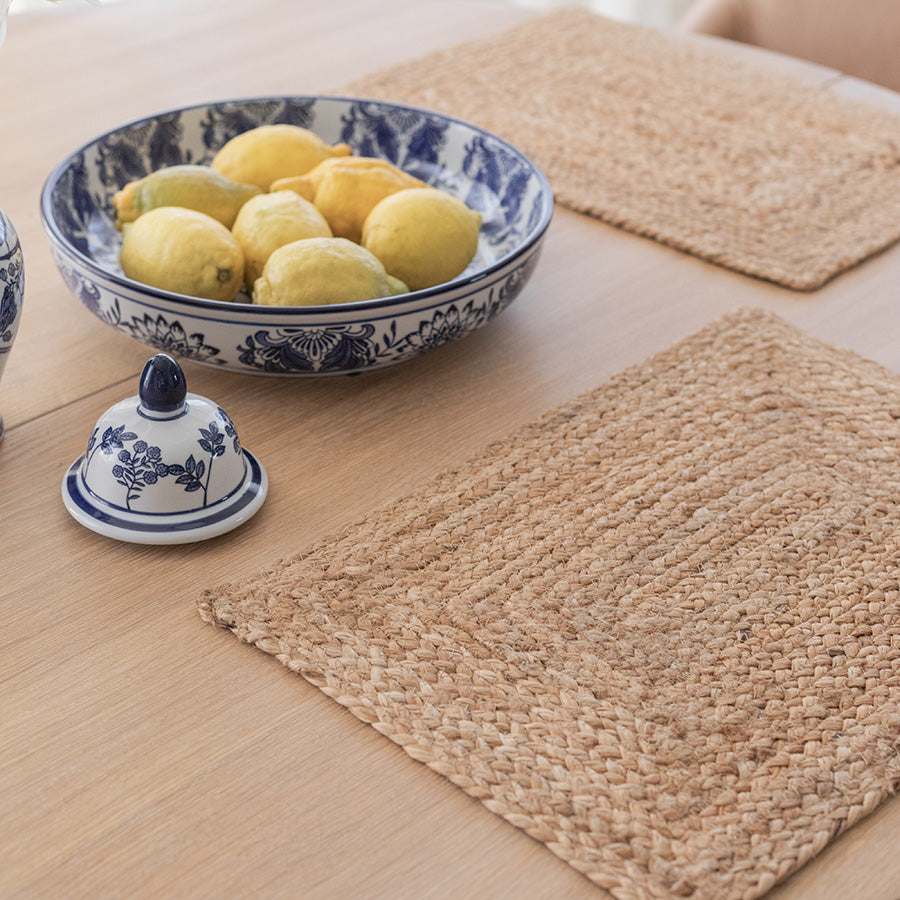 Nærbilde av en jute dekkebrikke på et spisebord med en keramisk skål fylt med sitroner, og en dekorativ tallerken i bakgrunnen.