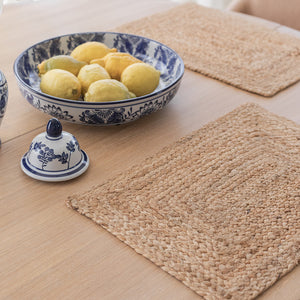 Nærbilde av en jute dekkebrikke på et spisebord med en keramisk skål fylt med sitroner, og en dekorativ tallerken i bakgrunnen.