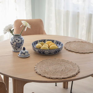Spisebord med jute dekkebrikker, dekorert med blomster, sitrona og keramikk for en koselig bordsetting.