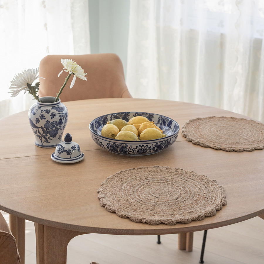 Spisebord med jute dekkebrikker, dekorert med blomster, sitrona og keramikk for en koselig bordsetting.