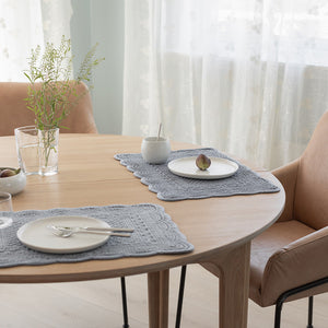 To dekkebrikker i quiltet velour på et rundt bord, sammen med tallerkener og glass, skaper et innbydende og moderne bordmiljø.