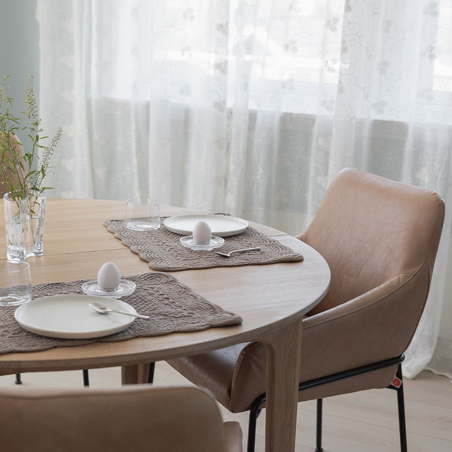 Dekkebrikke i velour i sandfarge på et rundt bord, satt for frokost med glass, tallerken og egg, omgitt av stilige stoler.