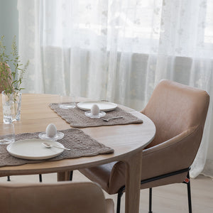 Dekkebrikke i velour i sandfarge på et rundt bord, satt for frokost med glass, tallerken og egg, omgitt av stilige stoler.