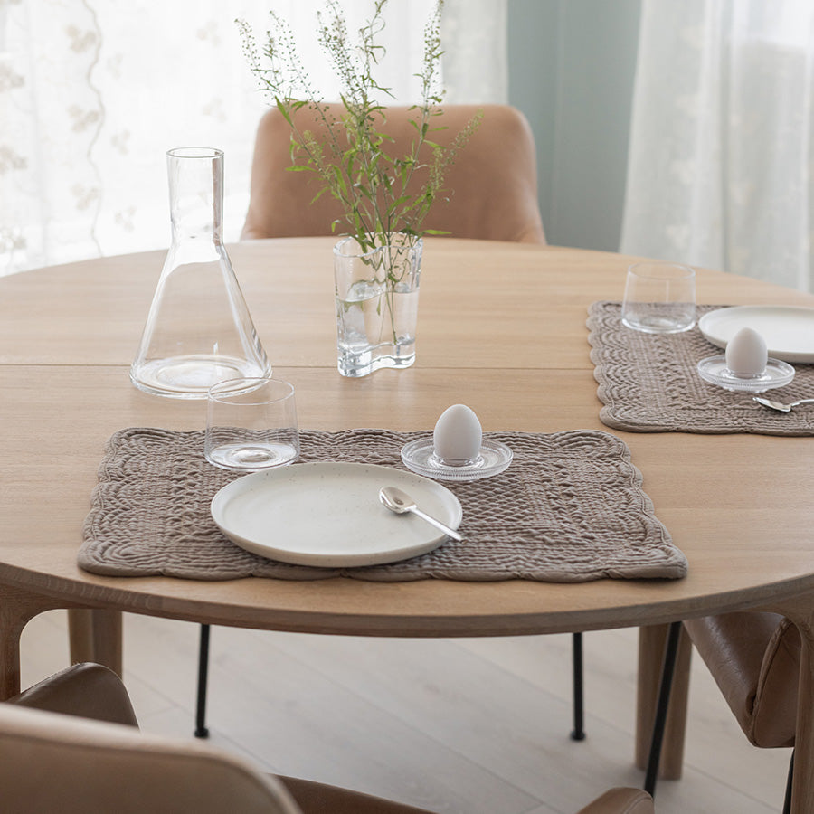 Dekkebrikke i sandfarget velour på et bord, pyntet med glass og en vase med blomster, gir en koselig atmosfære til middagsselskapet.