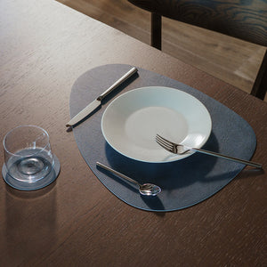 Borddekkingsbilde med mørk blå spisebrikke, tallerken, kniv, gaffel og glass.