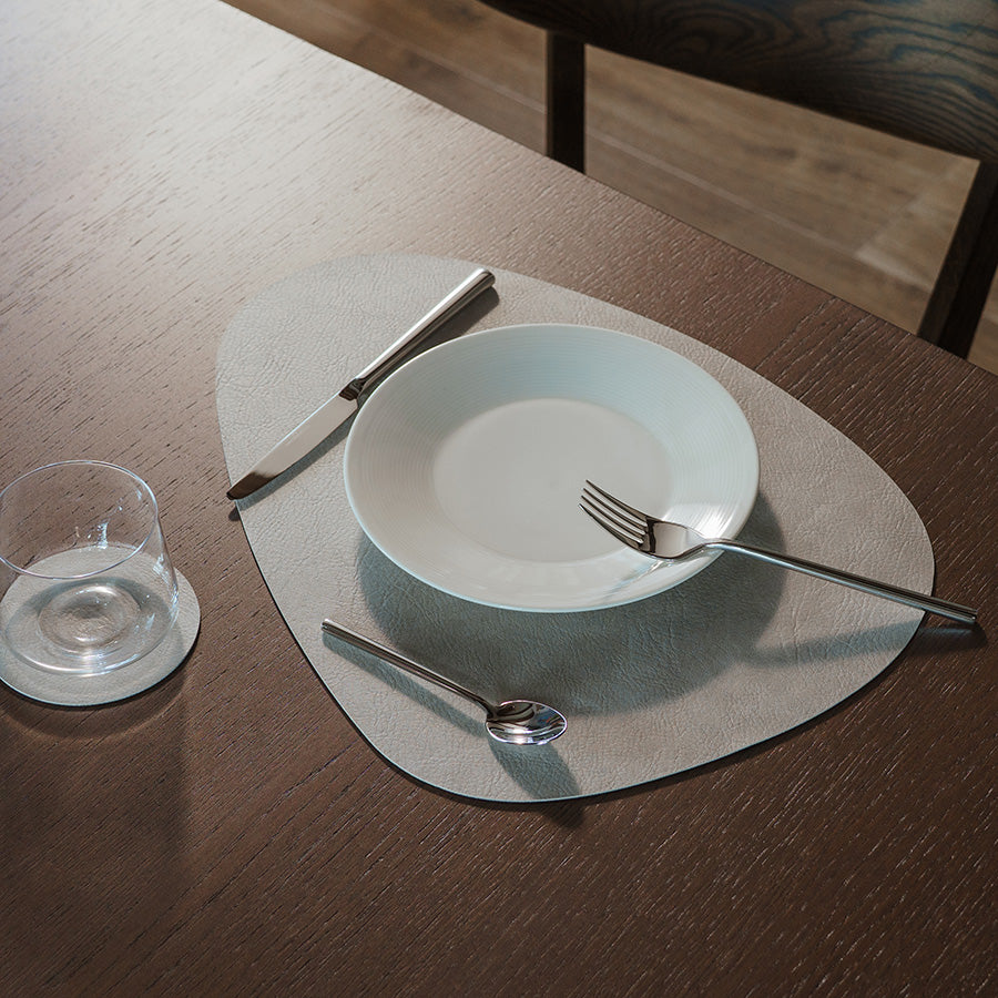 Borddekkingsbilde av spisebrikke i grå med tallerken og bestikk, perfekt for en elegant middag.