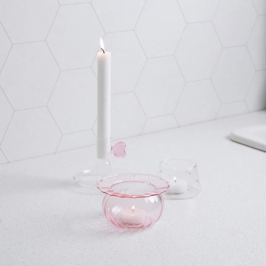 Lyslykt i klart glass med rosa detaljer, plassert på kjøkkenbenk med en hvit lysestake og annen dekor.