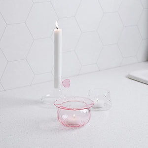 Lyslykt i klart glass med rosa detaljer, plassert på kjøkkenbenk med en hvit lysestake og annen dekor.