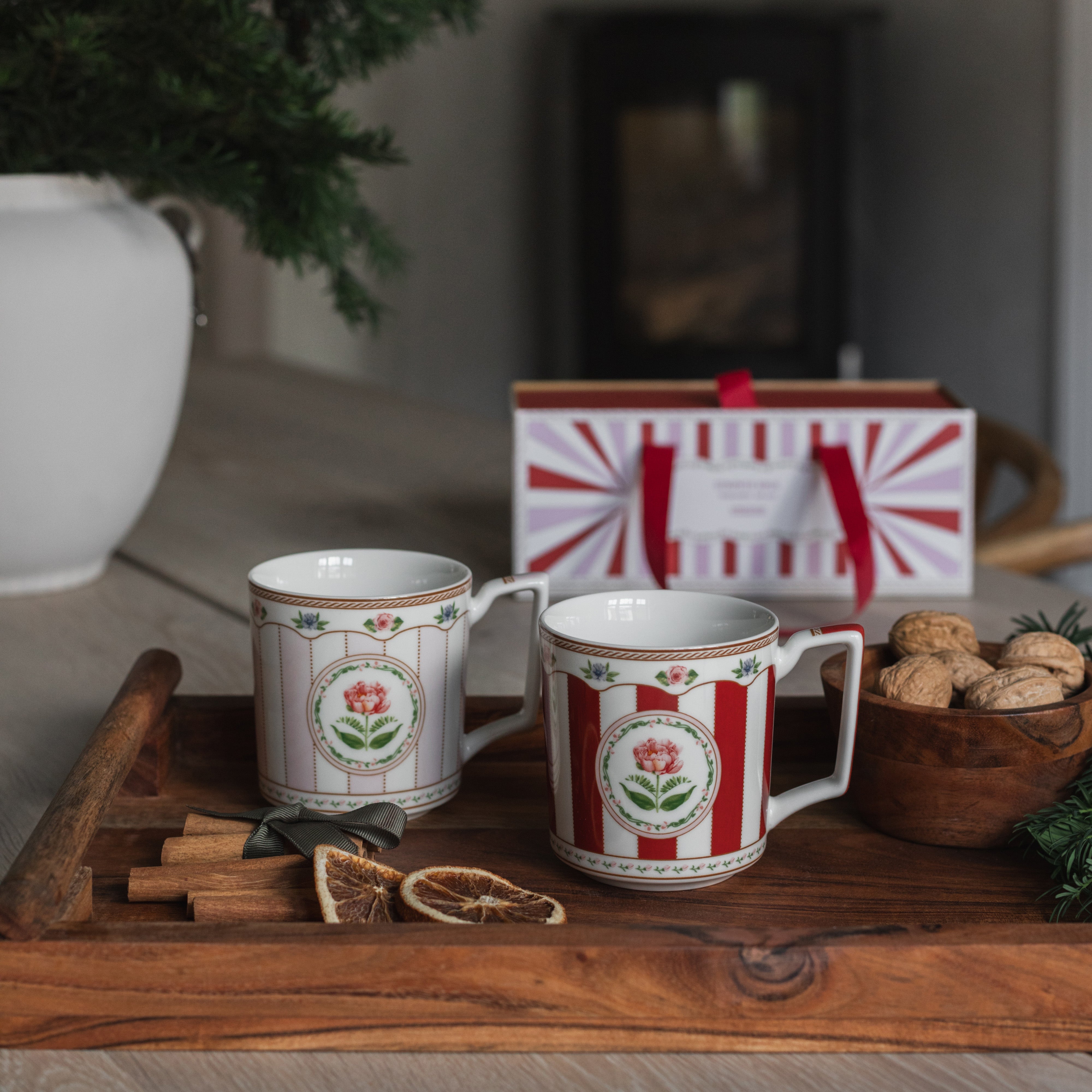 Rødt og rosa krus med rosemotiv på juledekket trebord, klare for kaffe eller te