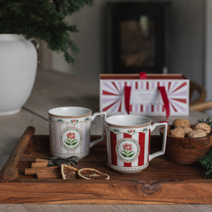Rødt og rosa krus med rosemotiv på juledekket trebord, klare for kaffe eller te