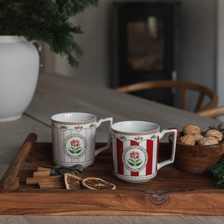 Rosa og rødt krus med elegant rosemotiv og gullkant i stemningsfull juleoppsett