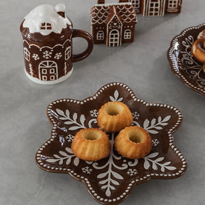 Pepperkakehus-krus med lokk ved siden av julefat med små formkaker og dekorative pepperkakehus