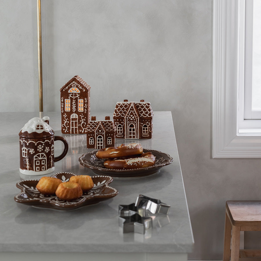 Juledekket bord med dekorativ tallerken, småkaker, pepperkakehus og matchende keramikk i pepperkakemotiv