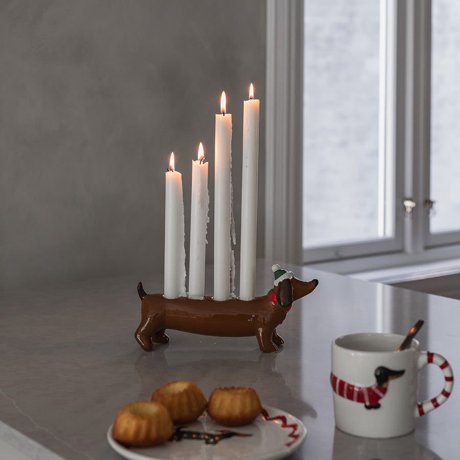 Keramisk dachshund lysestake med tente stearinlys på kjøkkenbenken, dekorert med julepynt og kaffekopp
