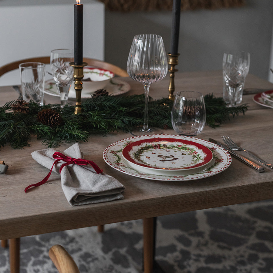 Juleglede tallerken med røde og grønne juledetaljer på elegant julebord med servise og lys