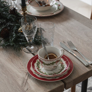 Juleglede kopp og skål med kaffe på juledekket trebord, omgitt av granbar, glass og bestikk