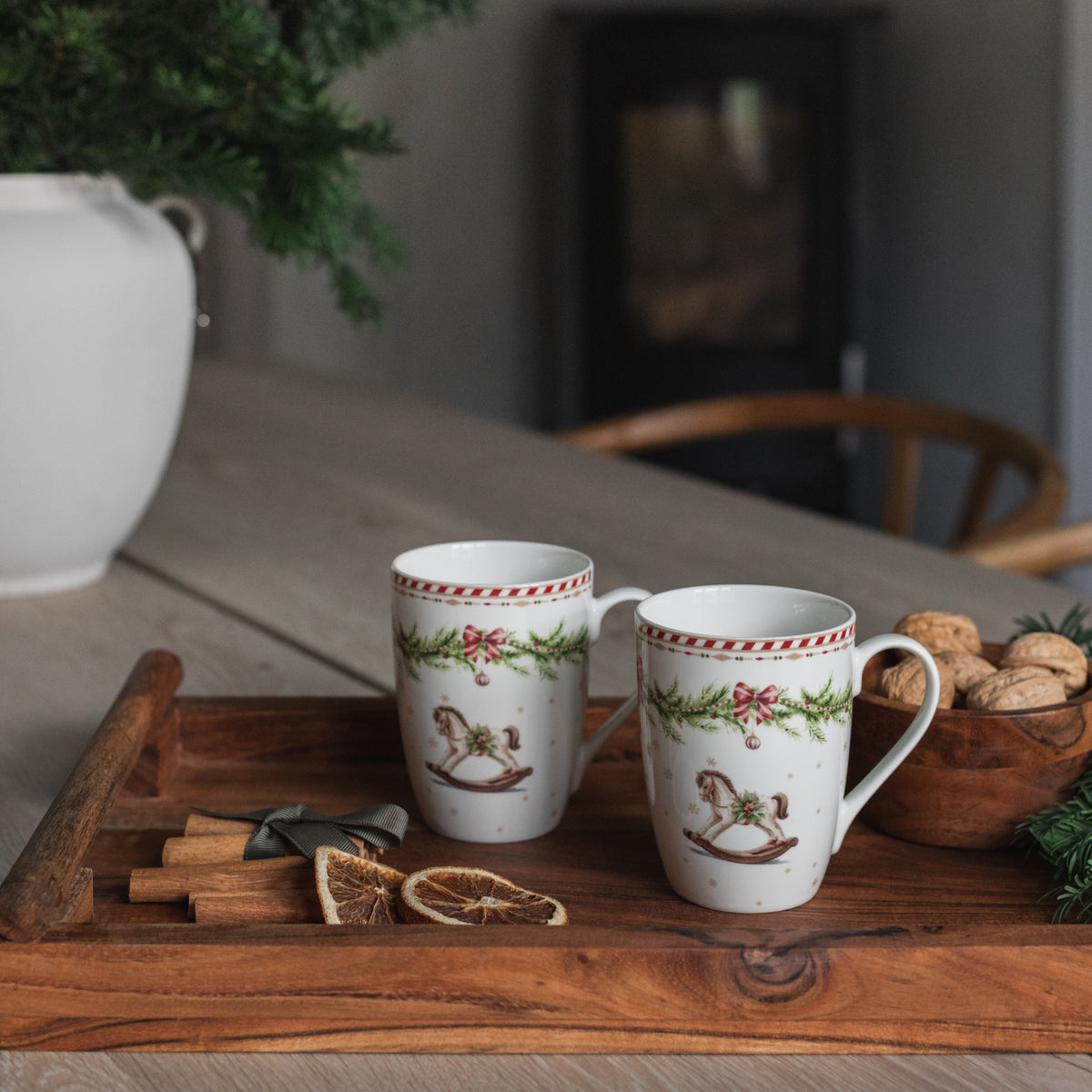 Juleglede krus i beinporselen med gyngehestmotiv, vist med kaffe på et stemningsfullt julebord
