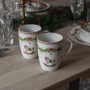 To Juleglede krus med julemotiv og gyngehest, dekorativt plassert på festdekket julebord