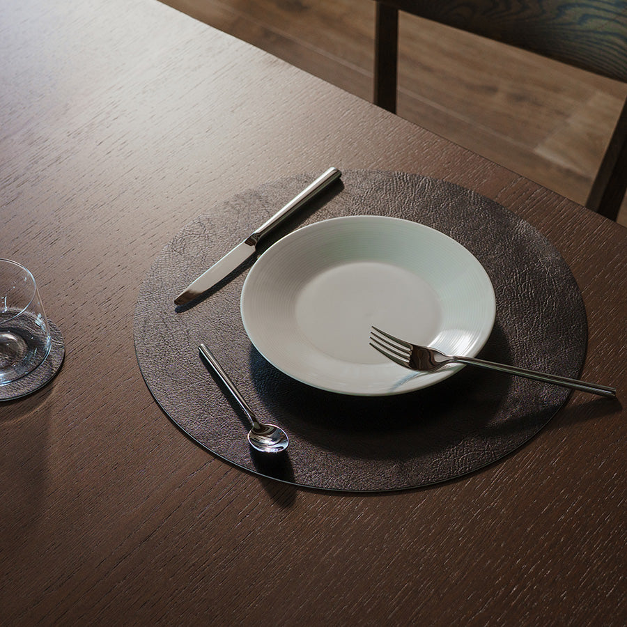 Spisebrikke i bruk på bord, med elegant dekking bestående av tallerken og bestikk, som viser den runde formen.