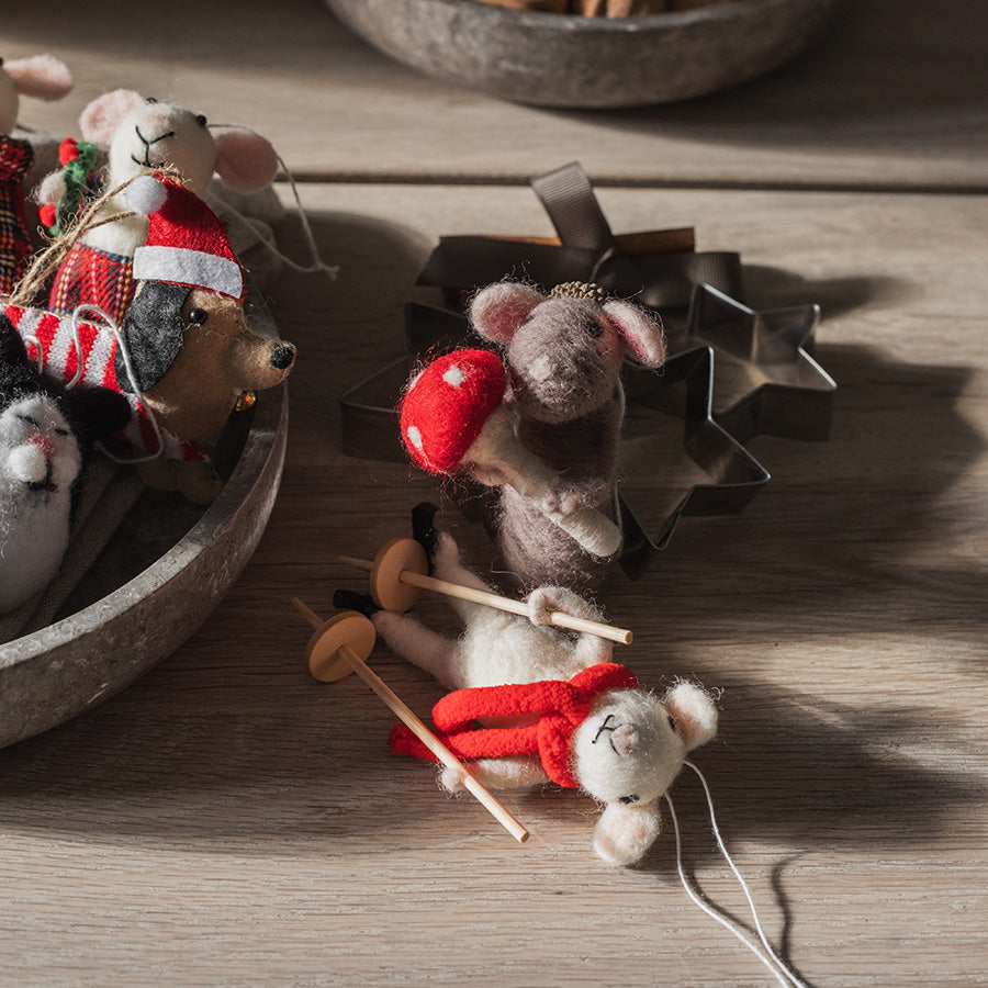 Tovede julemus som julepynt på trebord, med ski, sopp og dekorative julefigurer i bakgrunnen