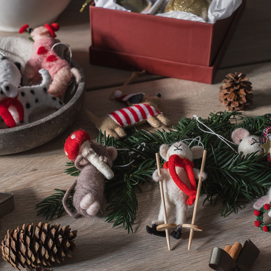 Julepynt med tovede mus på grankvist, én med sopp og én på ski, omgitt av kongler og juledekorasjoner