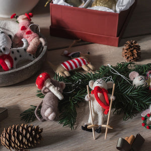 Julepynt med tovede mus på grankvist, én med sopp og én på ski, omgitt av kongler og juledekorasjoner