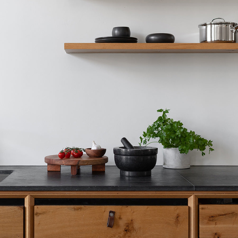 Classicpro morter i svart granitt plassert på en kjøkkenbenk med friske urter og tomater, perfekt for matlaging.