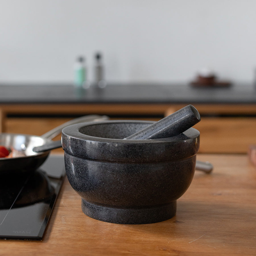 Classicpro morter stående på et trebord med et stekepanne i bakgrunnen, designet for effektiv knusing av ingredienser.