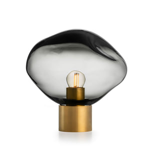 Elegant bordlampe fra Hadeland Glassverk, Crystal Stone i lys røkgrå, med en unik håndblåst kuppel, perfekt for å skape en sofistikert atmosfære i stuen eller soverommet.