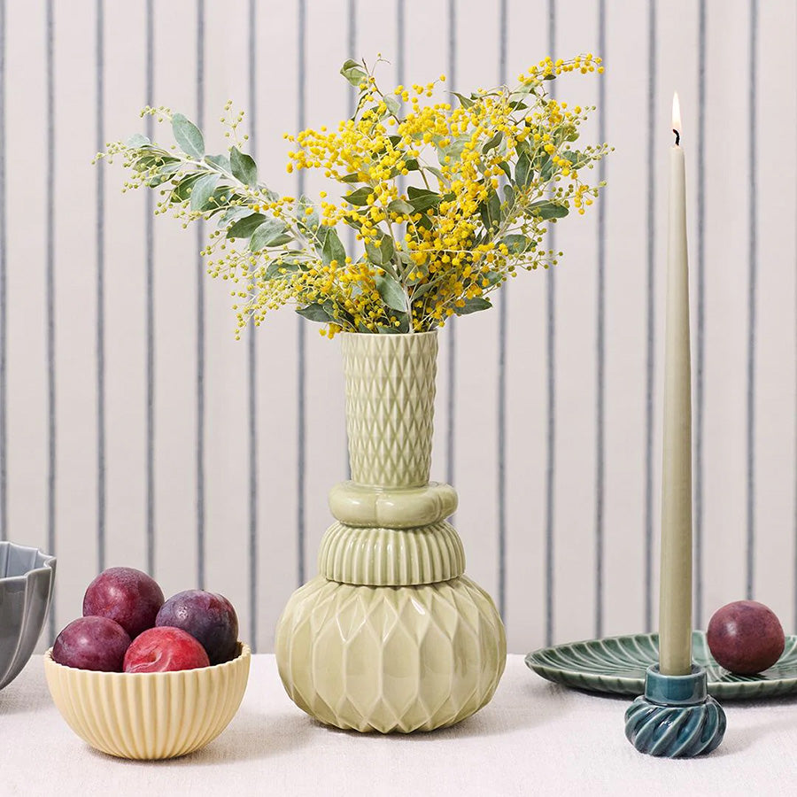 Dottir Nordic Design Samsurium Honkadonka vase med blomster, plassert på et bord med frukt og stearinlys, fremhever vase som både kunstverk og funksjonell innredning.