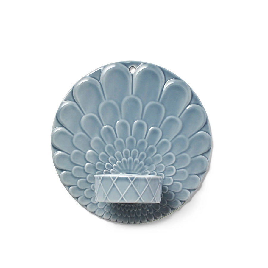 Pipanella Harlequin vegghengt telysholder i fargene blå og grå med kunstnerisk blomsterrelieff, designet for store telys, som skaper en stemningsfull belysning på veggen.