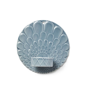 Pipanella Harlequin vegghengt telysholder i fargene blå og grå med kunstnerisk blomsterrelieff, designet for store telys, som skaper en stemningsfull belysning på veggen.