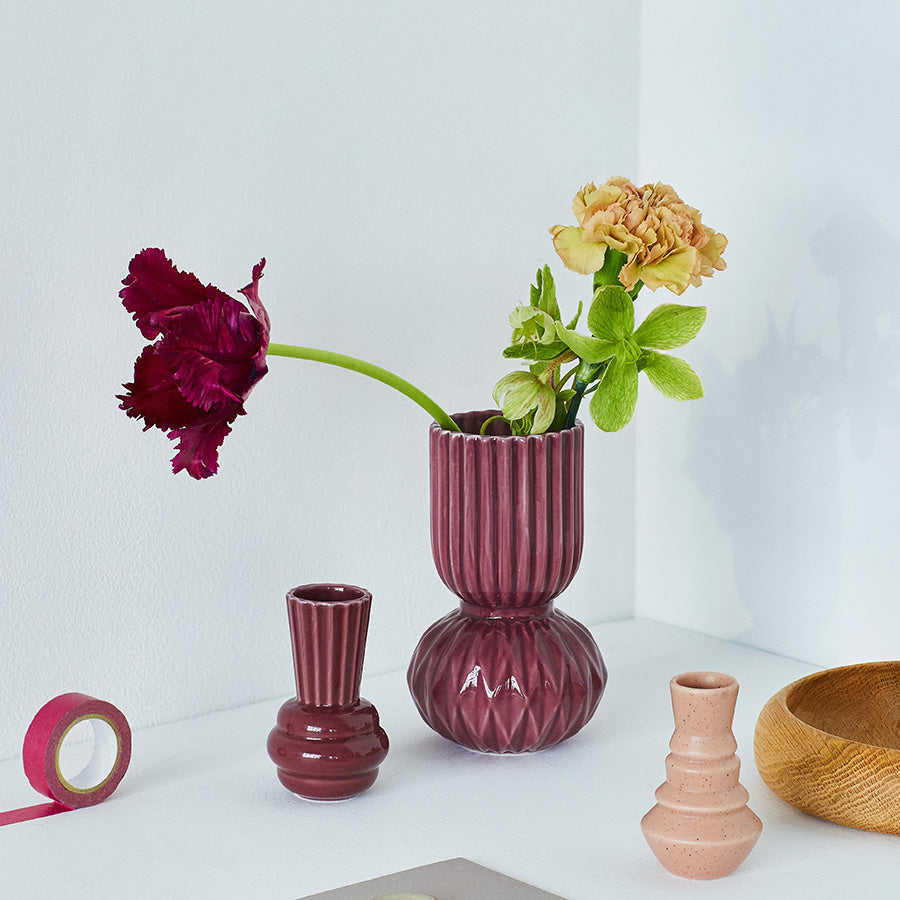 Dottir Nordic Design Samsurium Rufflebell Vase fylt med blomster, sammen med flere keramiske vaser og dekorative elementer på et bord.