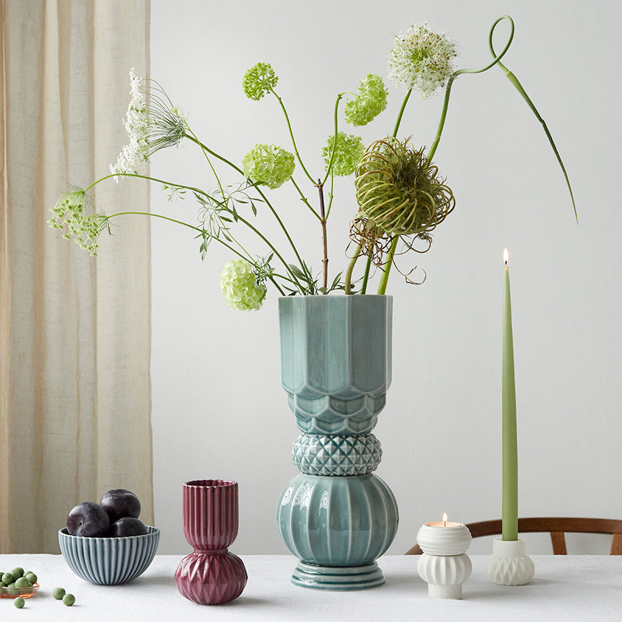 Samsurium Towerbell vase med blomster, plassert på et bord sammen med andre dekorative vaser og stearinlys. Elegant kombinasjon av stil og funksjon.