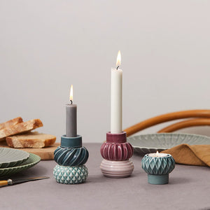 Elegante lysestaker fra Dottis Nordic Design plassert på et bord, med telys og kronelys i harmoniske nyanser av mørk, pudder og aubergine.