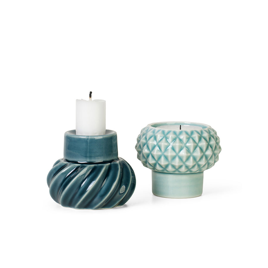 To keramiske lysestaker i petrol og peacock, en lysestake med telys og en med kronelys, ha et skulpturelt og modulært design.