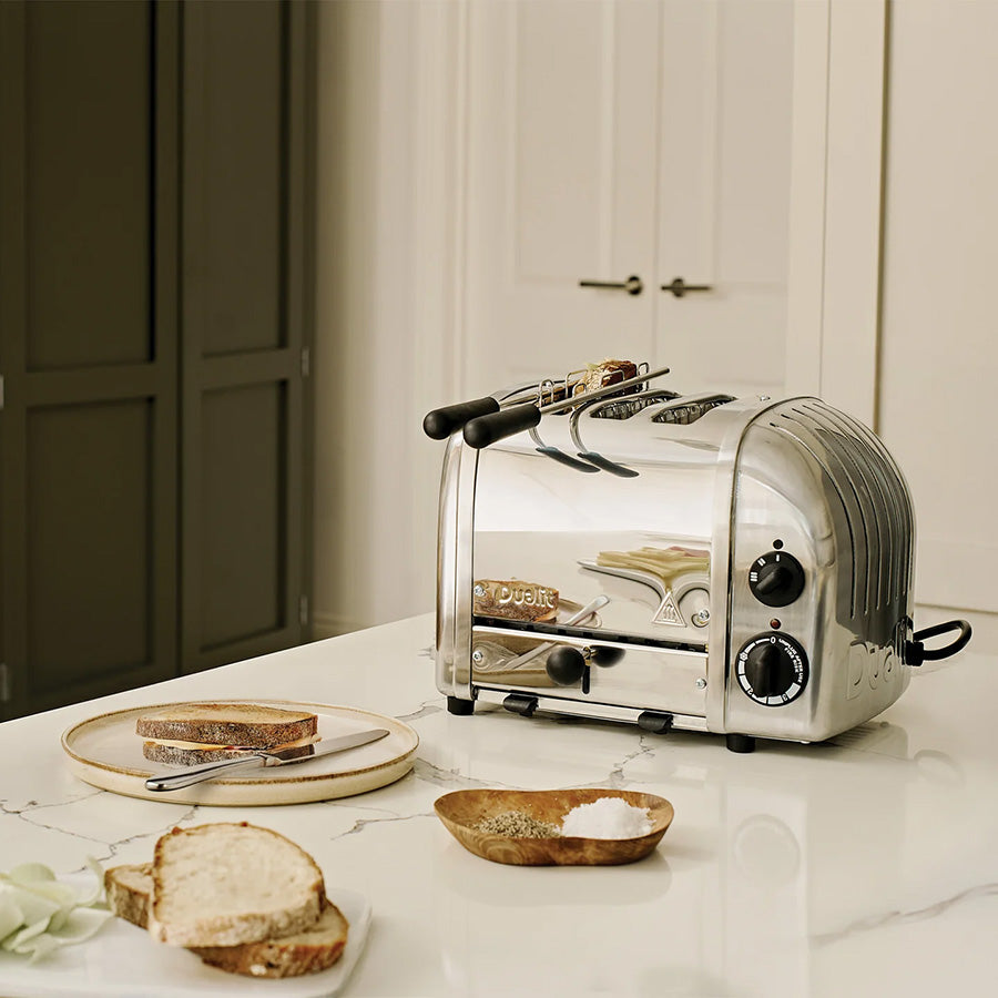 Dualit Classic brødrister står på et kjøkkenbenk med brødskiver ved siden av, perfekt for å tilberede frokost.