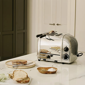 Dualit Classic brødrister står på et kjøkkenbenk med brødskiver ved siden av, perfekt for å tilberede frokost.