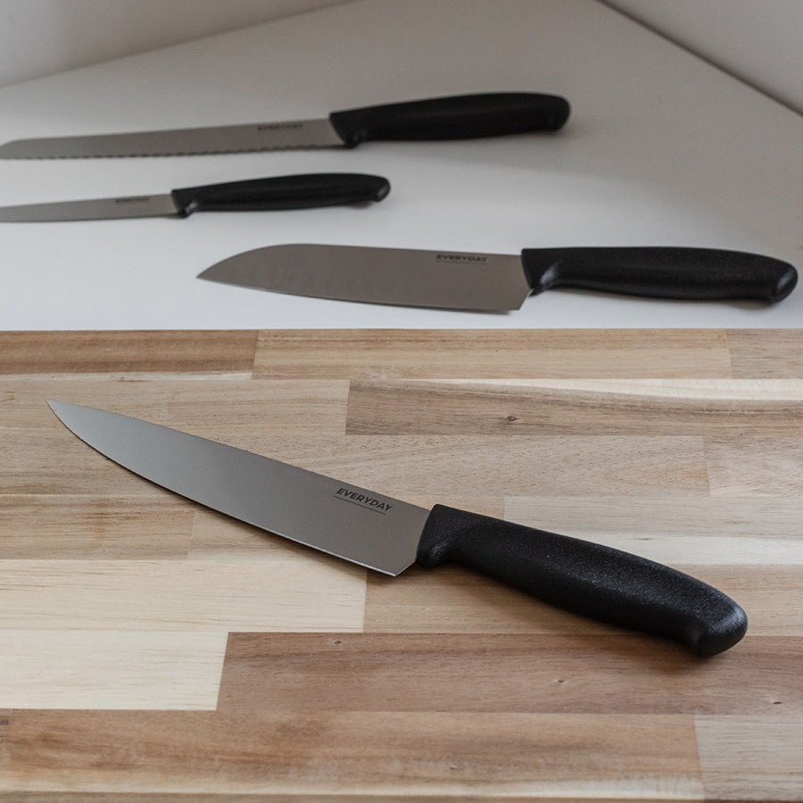 Everyday Cut kokkekniv 20 cm på kjøkkenbenk i tre med flere kniver fra serien i bakgrunnen