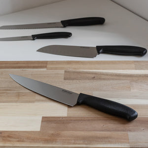 Everyday Cut kokkekniv 20 cm på kjøkkenbenk i tre med flere kniver fra serien i bakgrunnen
