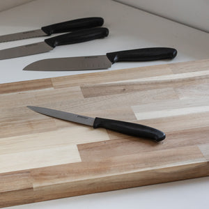 Everyday Cut universalkniv plassert på en skjærefjøl sammen med andre kniver, med fokus på det ergonomiske håndtaket.